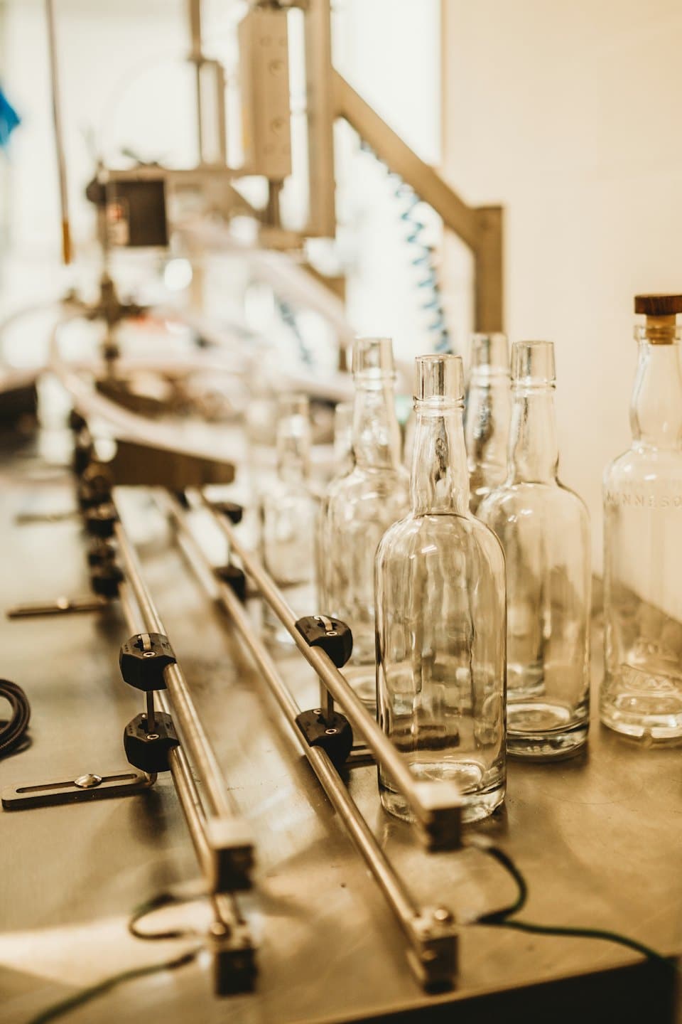 Clear glass bottles on a stainless steel conveyor belt in a factory.