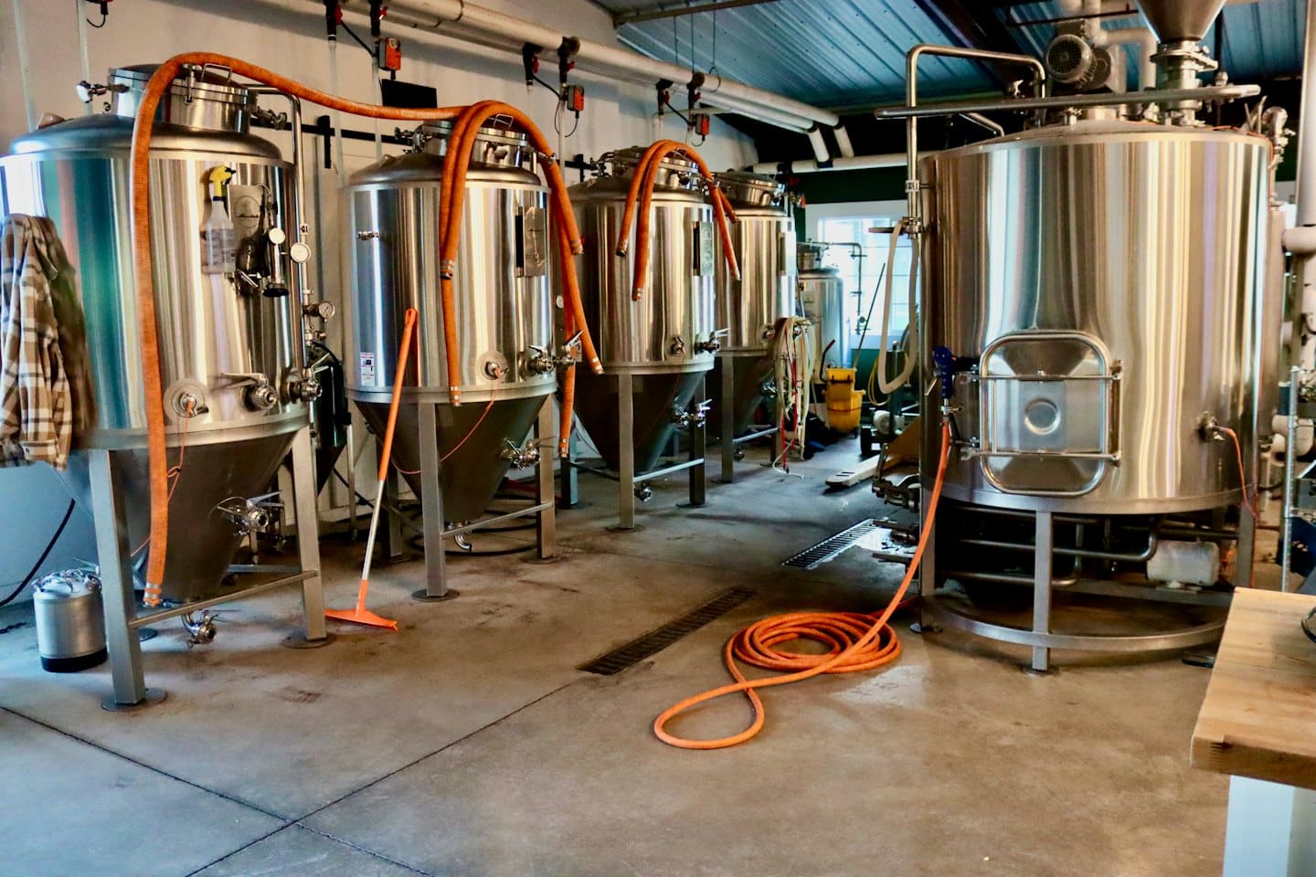 Stainless steel fermentation tanks stand inside a brewery production facility.