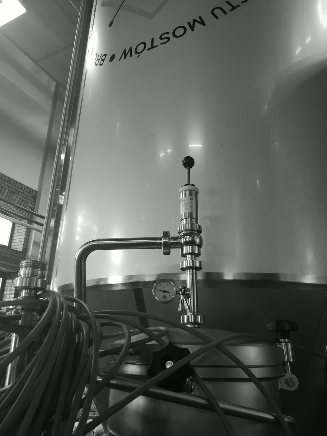 Shiny industrial fermentation tanks with piping inside a production facility.