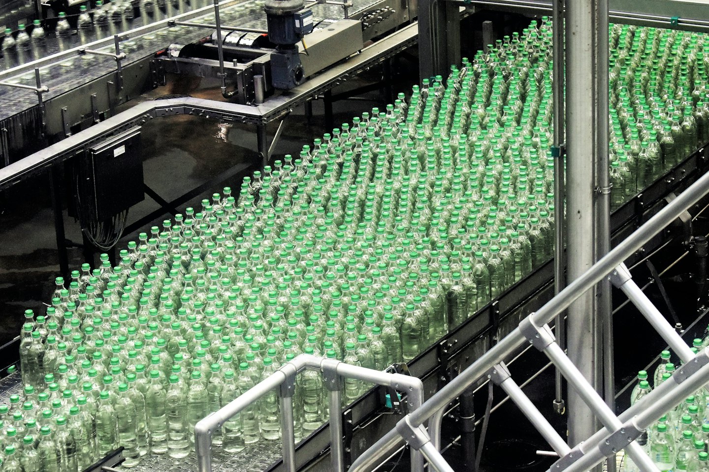 Plastic bottles with green caps on a conveyor belt in a factory.